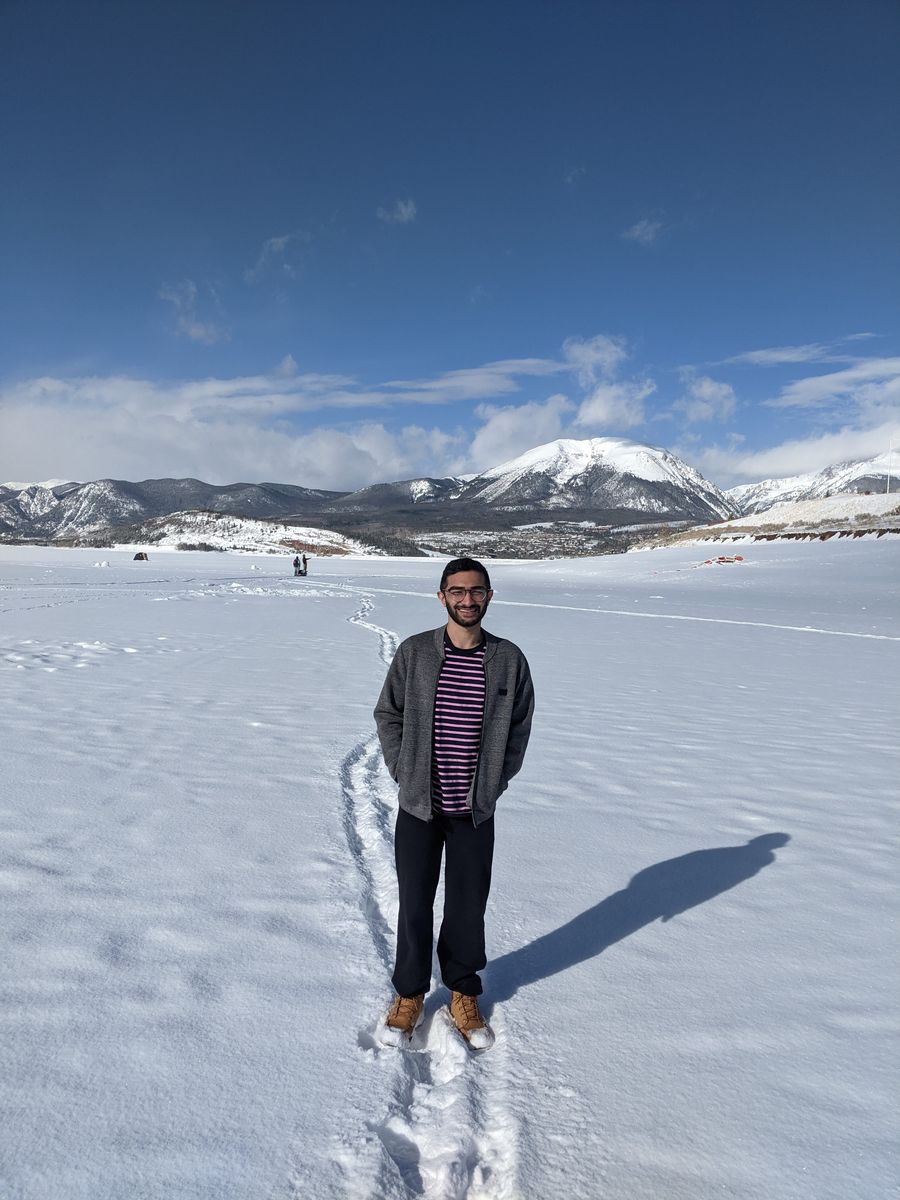 A man standing on a frozen snow-covered lake with snowy mountains behind
