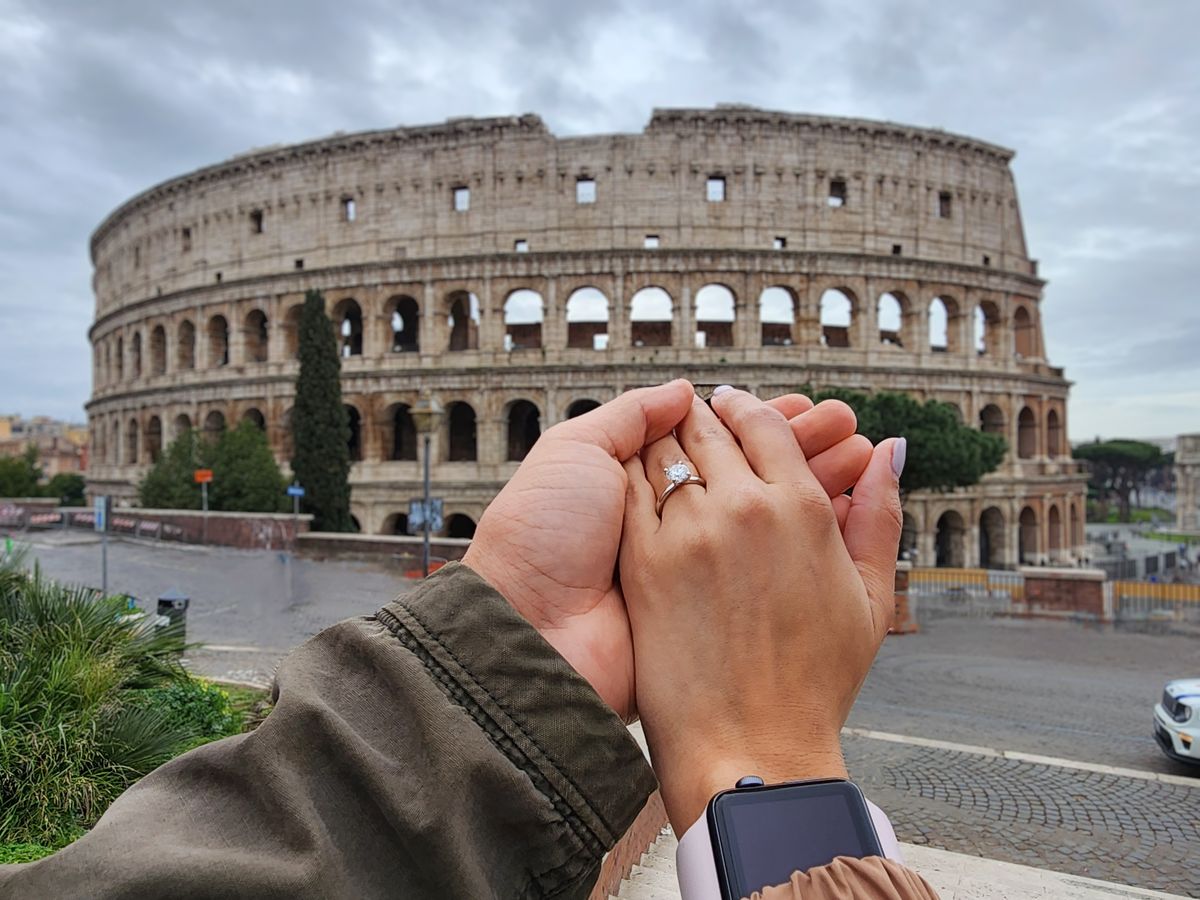 Clasped hands with an engagement ring before the Colosseum